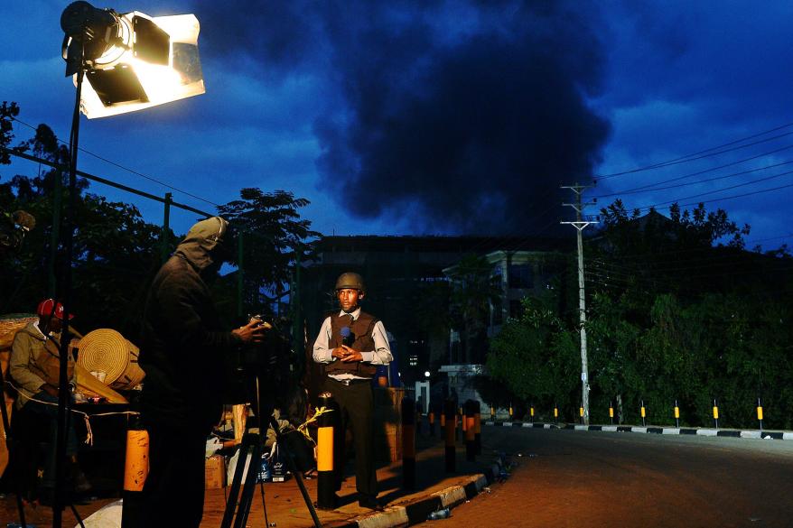 A Kenyan TV presenter stands in front of the rising smoke.