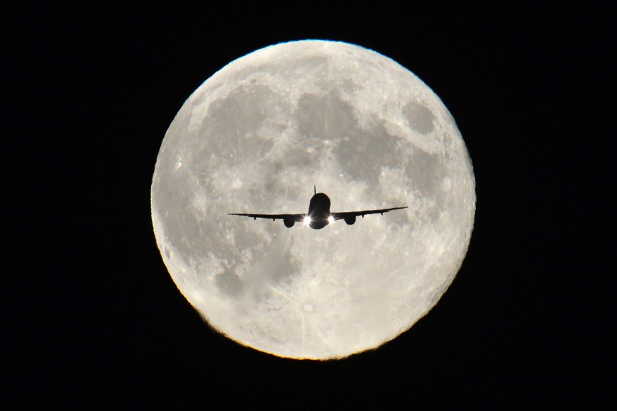 A passenger aircraft, with the full "Harvest Moon" seen behind, makes its final approach to landing at Heathrow Airport in west London