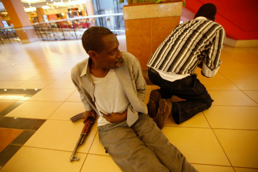 An injured policeman holds on to his wound as his compatriot searches through a shopping centre for gunmen in Nairobi