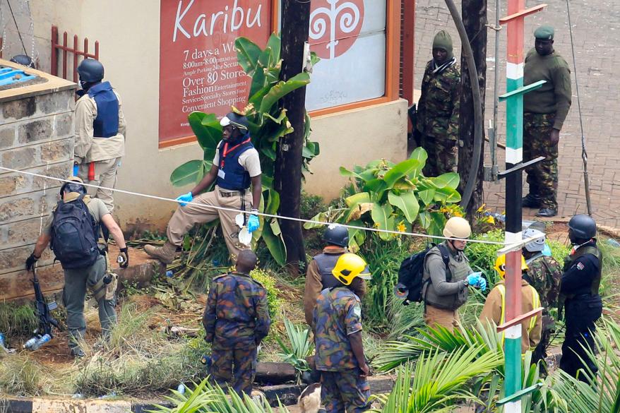 Foreign forensic experts, flanked by Kenyan military personnel check the perimeter walls around Westgate shopping mall in Nairobi.