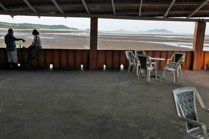 A couple talks inside an ocean front restaurant not far from where the New York Yankee pitcher Mariano Rivera played during his childhood in his hometown of Puerto Caimito, Panama. His childhood friends like Alfred Munoz remember how Rivera hated to lose. When his team was behind in a game, he'd throw the ball into the ocean and call it a tie.