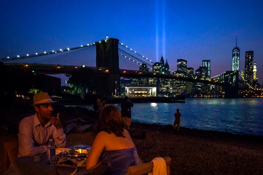 A couple enjoys dinner over looking the Brooklyn Bridge as the Tribute in Light illuminates the sky over the Lower Manhattan skyline a day ahead of the 12-year anniversary of the 9/11 attacks in the Brooklyn borough of New York