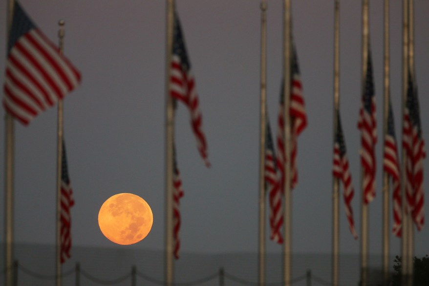 Full Moon Sets Behind Flags Lowered To Half Staff