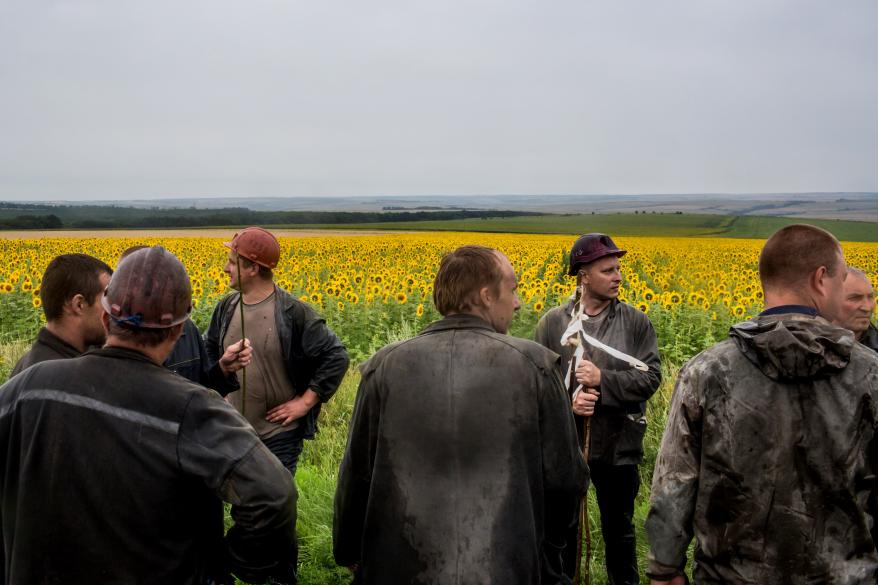 A group of miners rest after searching for debris and human remains in a sunflower field.