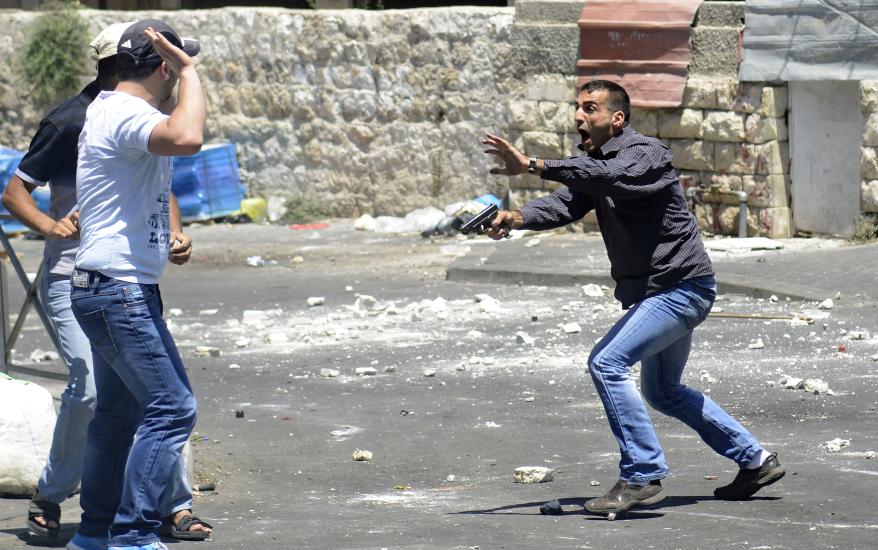 An undercover Israeli police officer with a gun speaks to bystanders to move, as other officers were trying to detain a Palestinian man