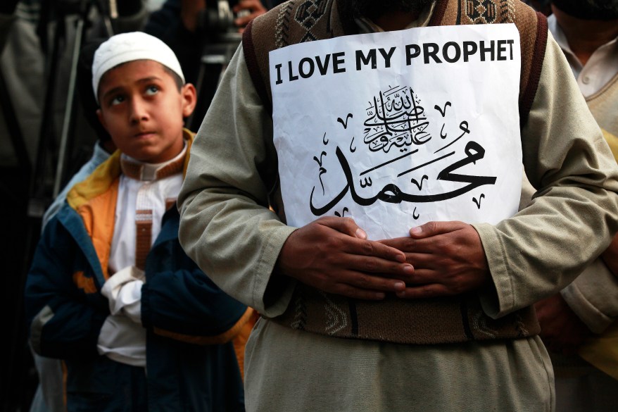 A boy looks on as a supporter of a religious group holds a sign which reads "Mohammad", during a protest against against satirical French weekly newspaper Charlie Hebdo, which featured a cartoon of the Prophet Mohammad as the cover of its first edition since an attack by Islamist gunmen, in Lahore January 23, 2015. REUTERS/Mohsin Raza (PAKISTAN - Tags: POLITICS CIVIL UNREST TPX IMAGES OF THE DAY RELIGION MEDIA)