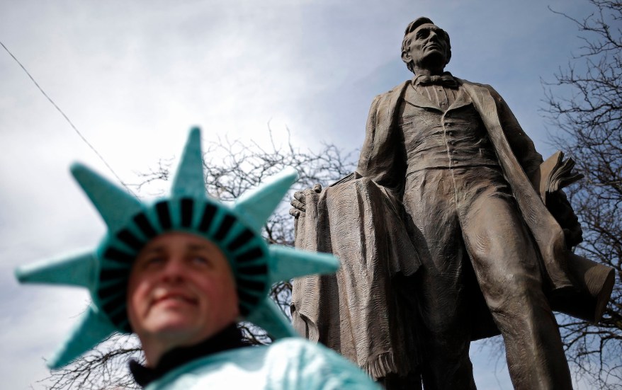 A man dressed as the Statue of Liberty poses in front of a Lincoln statue in Chicago.