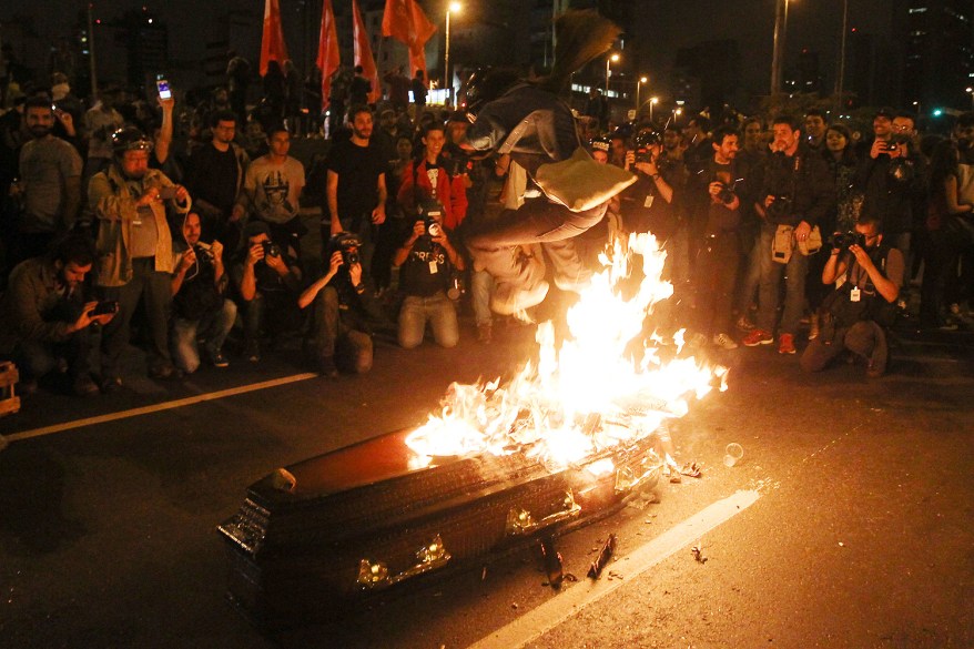 An anti-government protester jumps over a coffin that represents a symbolic funeral of Brazil's President Michel Temer in Sao Paulo, Brazil.