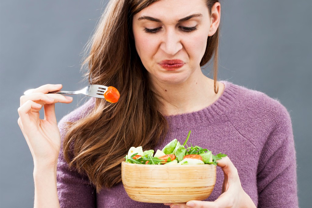 displeased young girl being picky at eating mixed green salad with cherry tomatoes as vegetarian diet