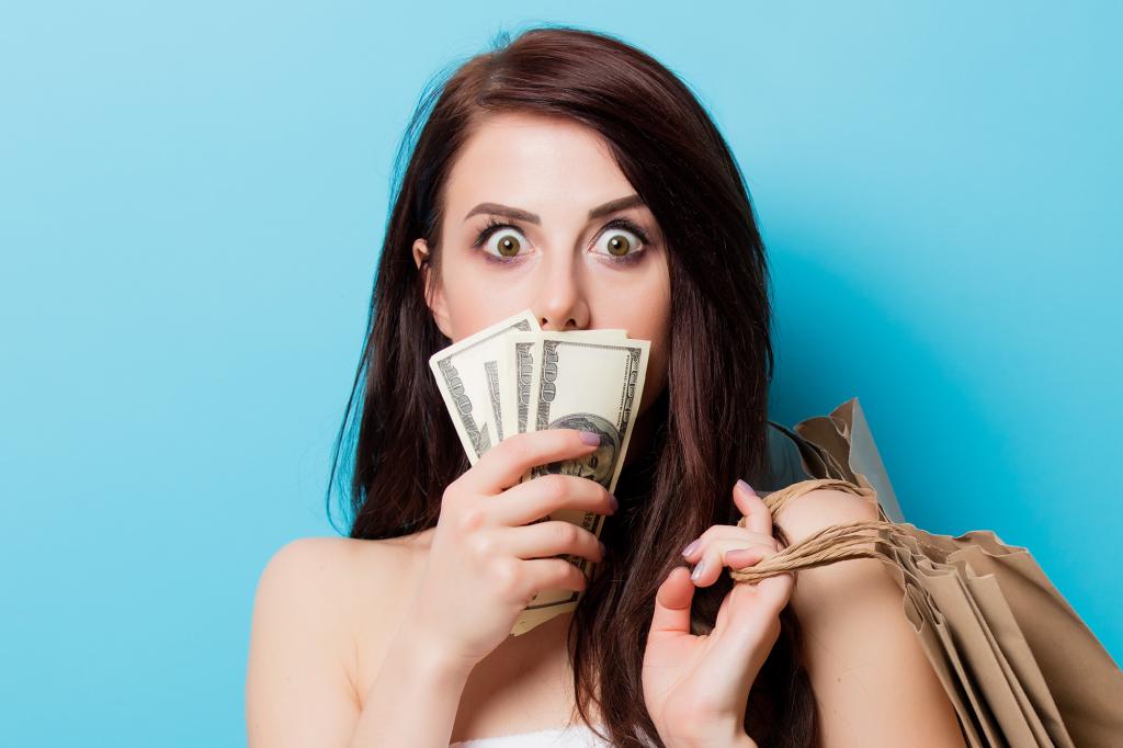 beautiful young woman with shopping bags and money standing in front of wonderful blue background