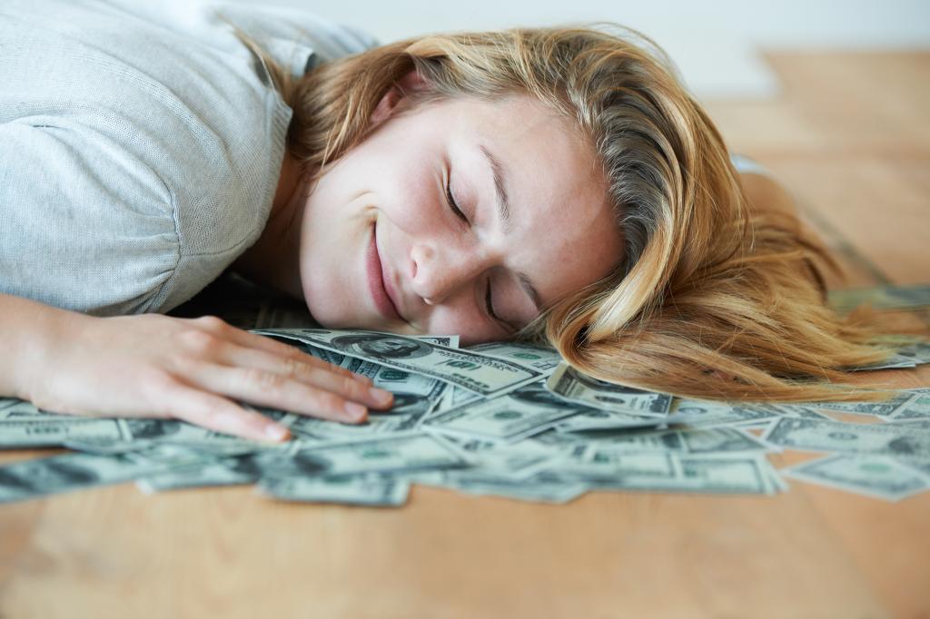 A girl smiles while lying down on a pile of money.