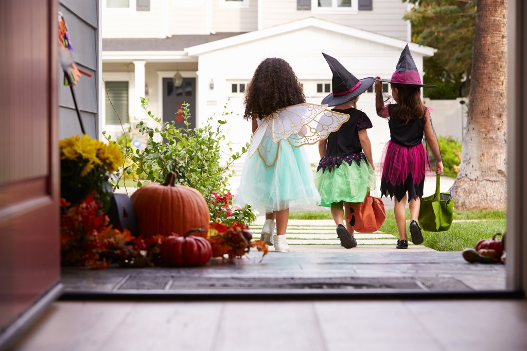 Three Children In Halloween Costumes Trick Or Treating