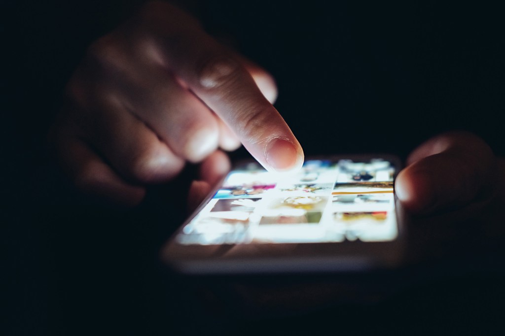 Person scrolling through apps on their smartphone in the dark.