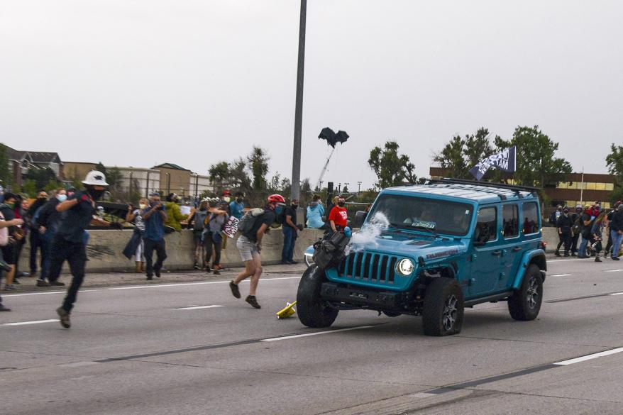 People run to get out of the way as a Jeep speeds through a crowd of people protesting the death of Elijah McClain on Interstate 225 in Aurora, Colorado.