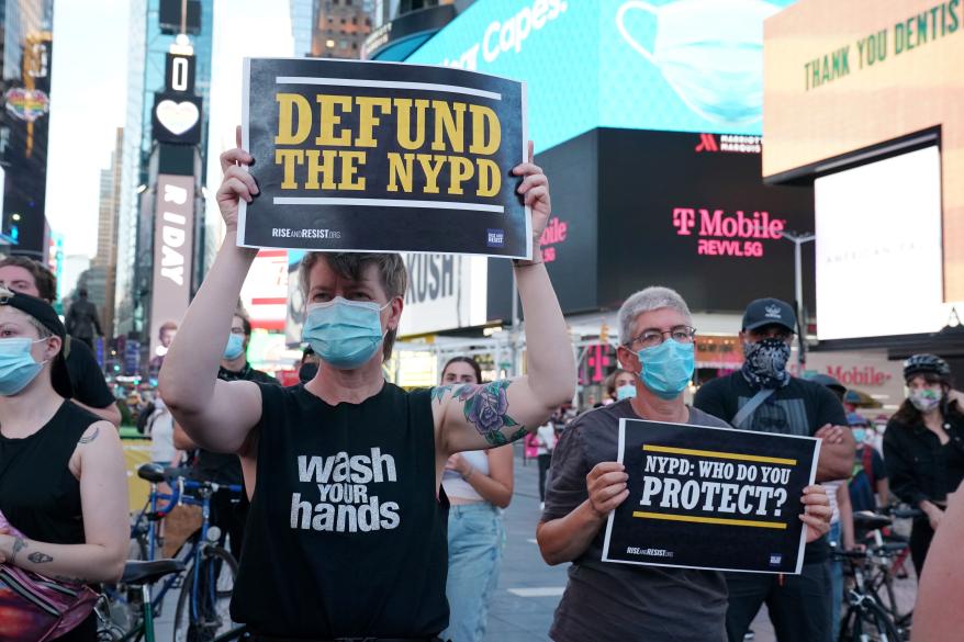 Protesters holding "defund the NYPD" signs in Times Square