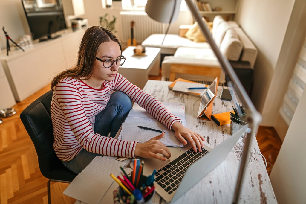 A teenage girl studying online using laptop at home.
