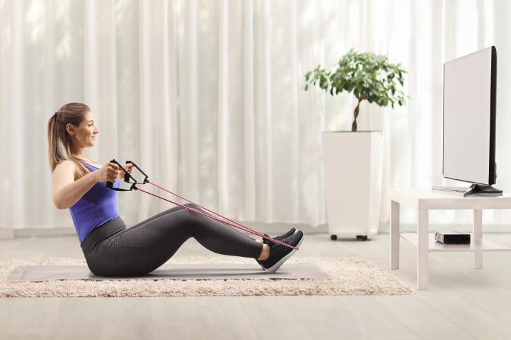 Woman sitting on the floor and exercising with a resistance band in front of a tv