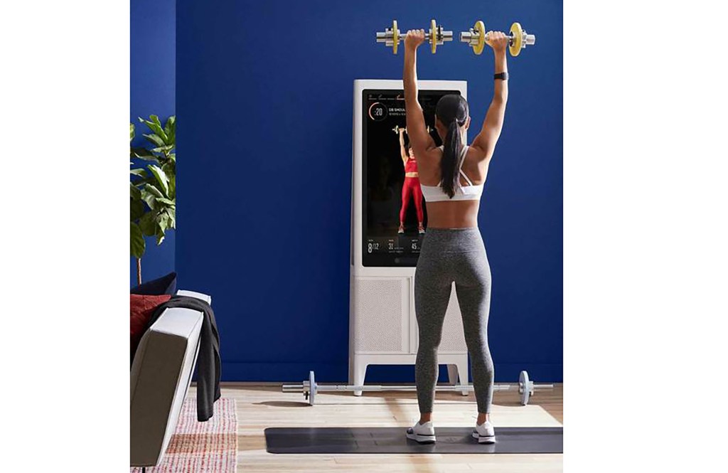 A woman uses a Tempo fitness device in her home, lifting weights 