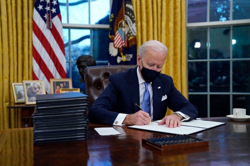 President Joe Biden signs his first executive order in the Oval Office.