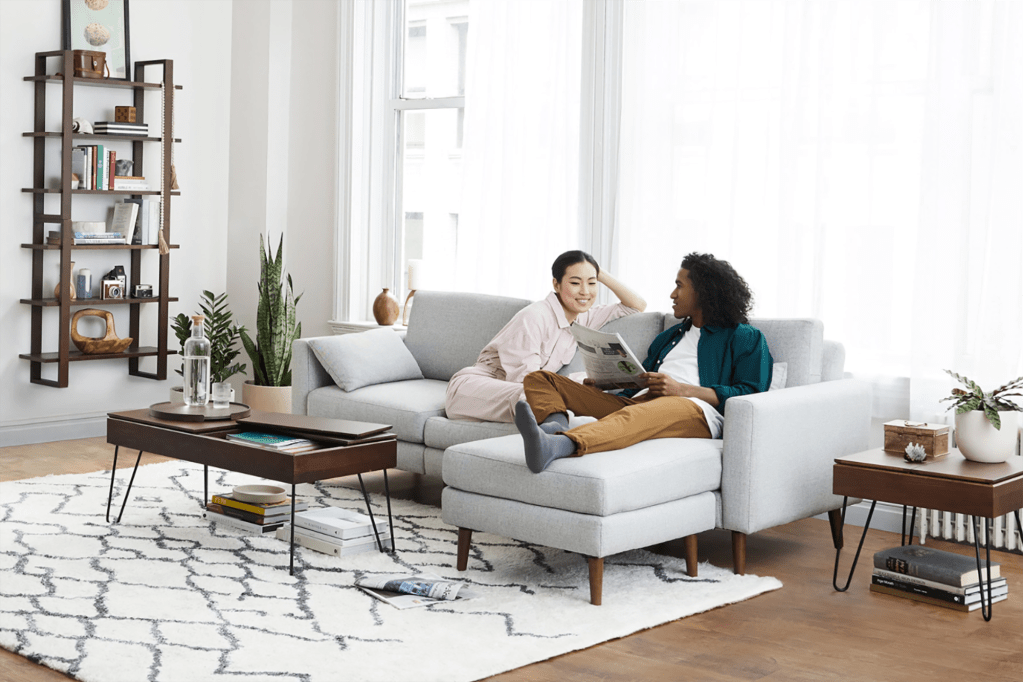 A man and a woman sit on a gray couch in a nicely decorated living room 