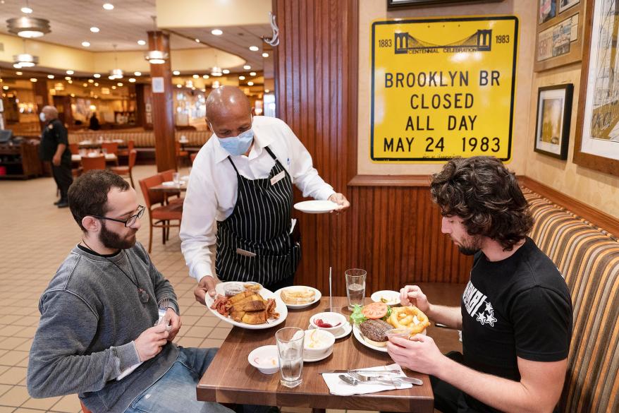 Waiter Lenworth Thompson serves lunch to David Zennario (left) and Alex Ecklin at Junior's Restaurant.