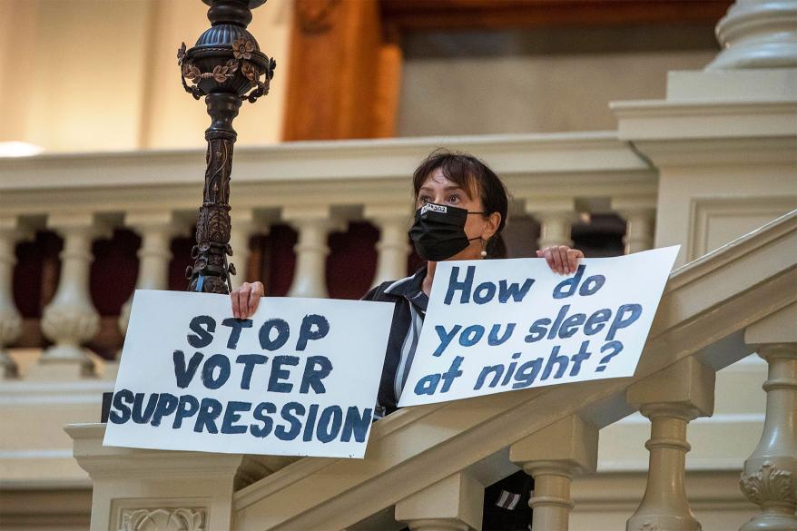 Ann White of Roswell holds protest signs on the North Wing stairs of the Georgia State Capitol building on day 38 of the legislative session in Atlanta, Thursday, March 25, 2021.