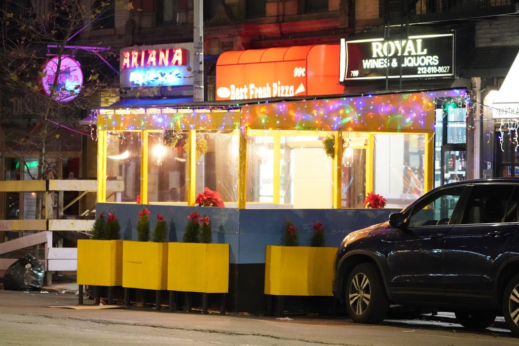 A car parked next to an outdoor dining enclosure.