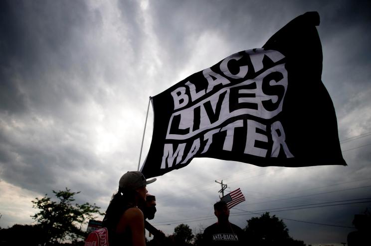 Black Lives Matter supporters waving the flag through the wind as protesters demonstrate along Miller Road outside of a Target, Tuesday, May 25, 2021