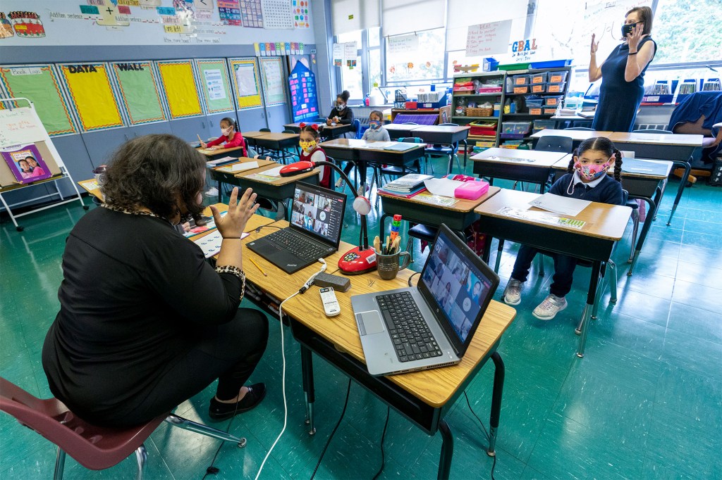 This file photo from Tuesday, Oct. 20, 2020, shows first-grade teacher Megan Garner-Jones, left, and Principal Cynthia Eisner silent clap for their students participating remotely and in-person at School 16, in Yonkers, N.Y.