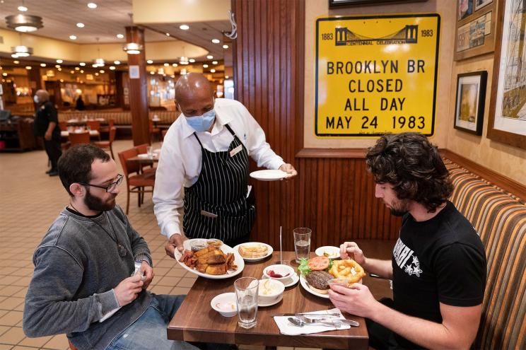 In this Sept. 30, 2020 file photo, Waiter Lenworth Thompson serves lunch to David Zennario, left, and Alex Ecklin at Junior's Restaurant in New York.