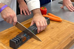 A pair of hands holding a knife and sharpening it on a cutting board