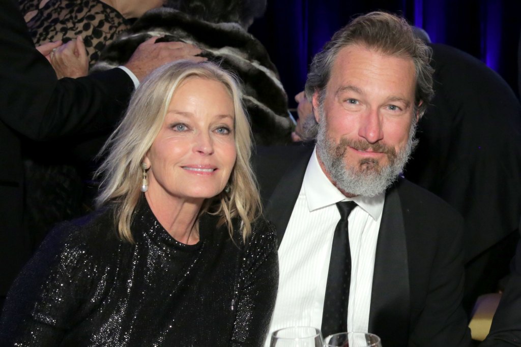 Bo Derek in black and John Corbett in a dark suit attend an event. 