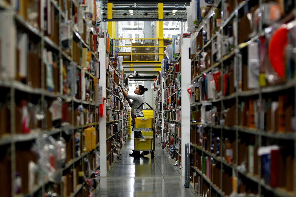 An Amazon warehouse worker taking an object off of a shelf.