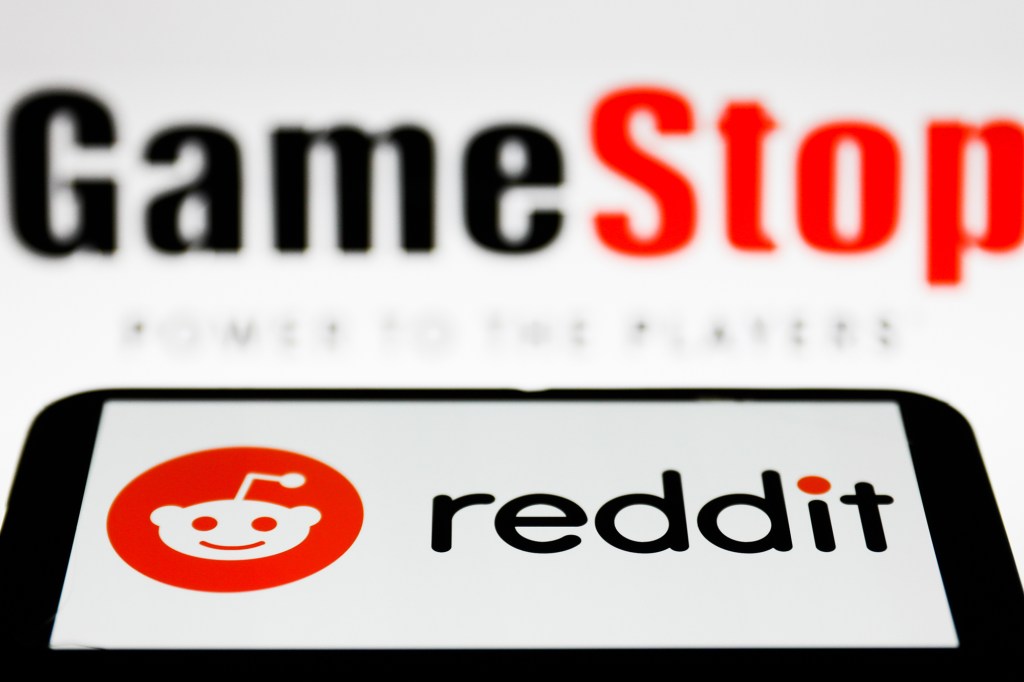 Reddit logo is displayed on a smartphone with a GameStop logo in the background in this photo illustration