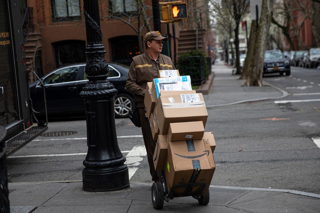 UPS delivery man pushing down a street a dolly stacked with packages 