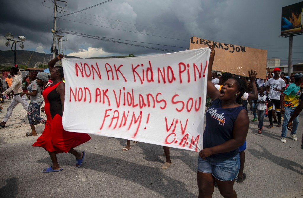 People protest carrying a banner with a message that reads in Creole: "No to kidnappings, no to violence against women ! Long live Christian Aid Ministries,"  demanding the release of kidnapped missionaries.