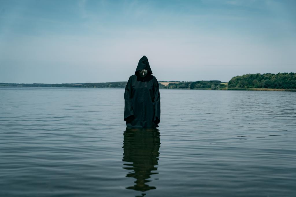 A creepy ghost in a black cloak standing in the water during the afternoon