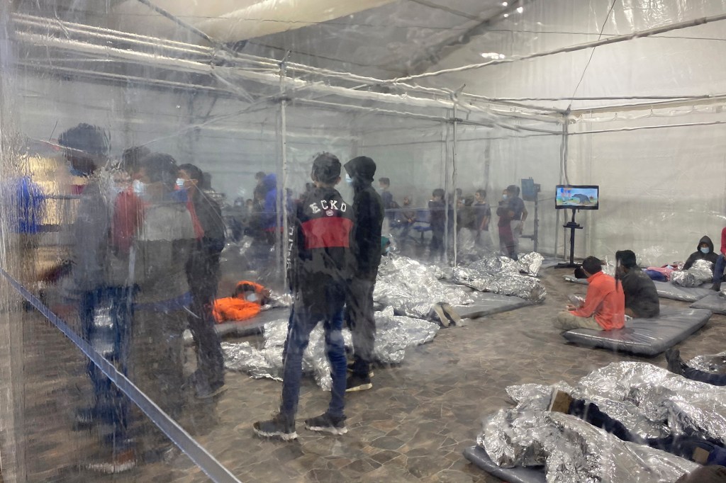 Immigrant detainees are seen behind a clear divider in a tented room.