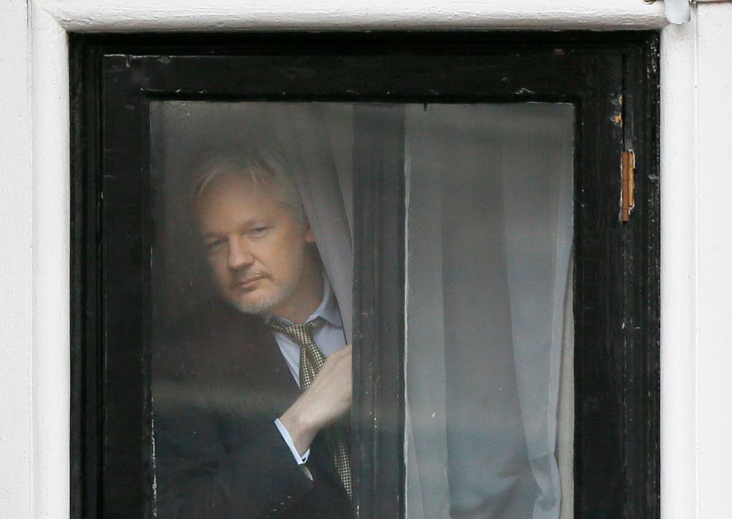 Julian Assange peeking out from behind a window pane.