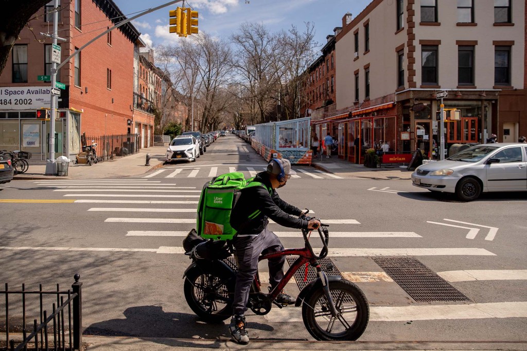 An Uber Eats bicycle delivery worker crossing a street.