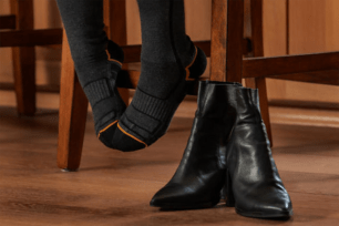 A woman's feet in gray and orange socks and a pair of black bootie shoes