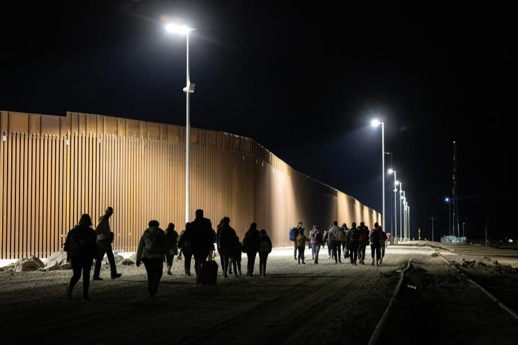 Immigrants walk along the U.S. border wall after crossing from Mexico through a nearby gap in the fence on December 07, 2021 in Yuma, Arizona.