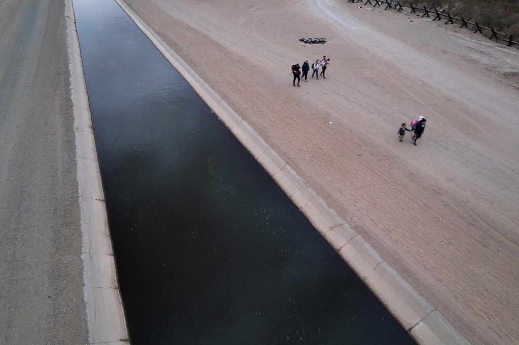 In an aerial view, Immigrants walk along an irrigation canal towards a makeshift encampment after crossing into the U.S. from Mexico through a gap in the border wall on December 10, 2021 in Yuma, Arizona.