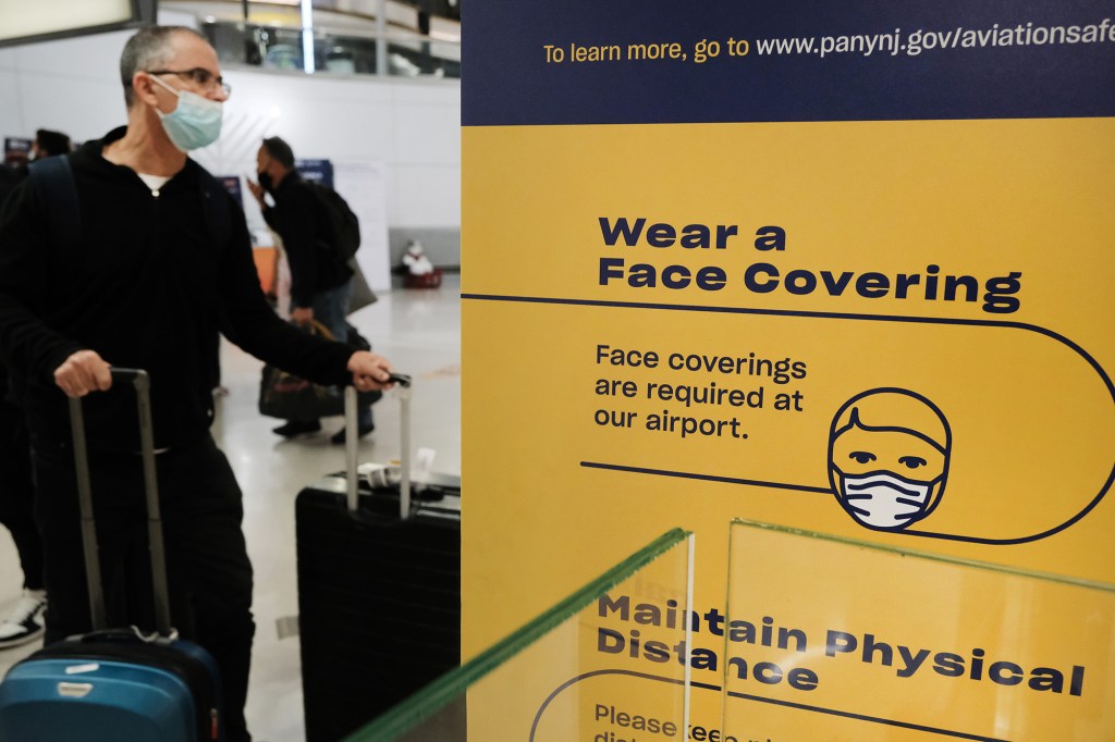 Man wearing a mask standing near a sign at an airport advising travelers to wear a face cover