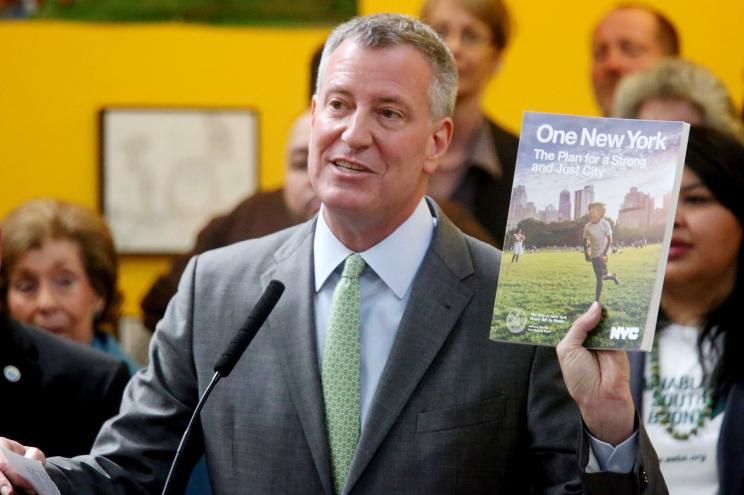 Mayor Bill de Blasio holds up pamphlet for "One New York: The Plan for a Strong and Just City" at a Bronx press conference.