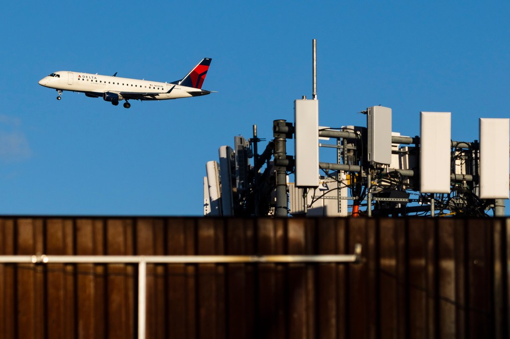 A Delta airlines airplane on approach to land at LaGuardia Airport passes telecommunications antennae on a rooftop in Queens.