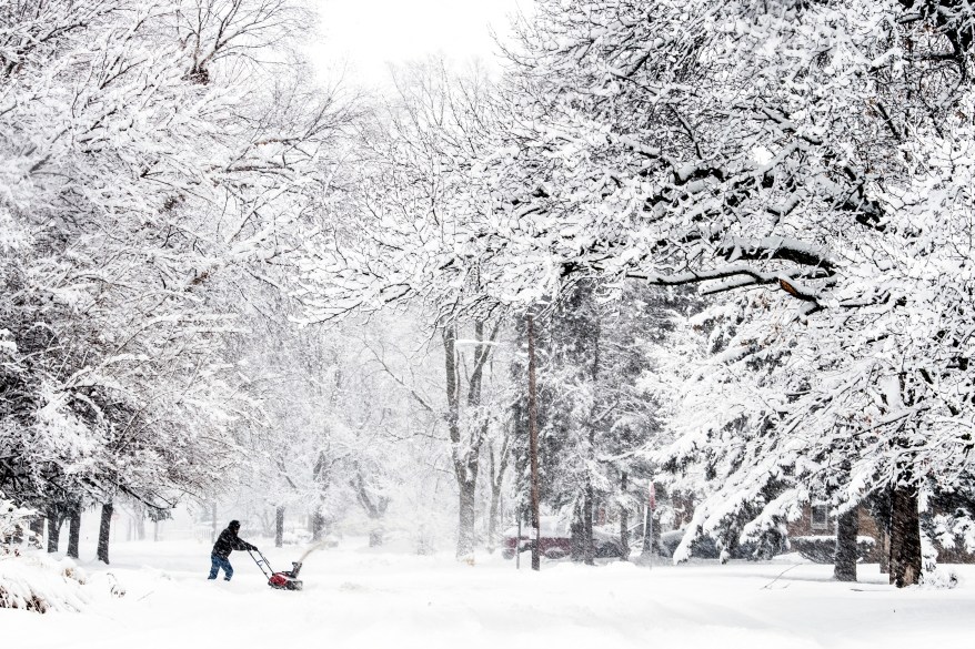 A resident uses a snowblower to clear out his driveway on February 2, 2022, in downtown Flint, Michigan.