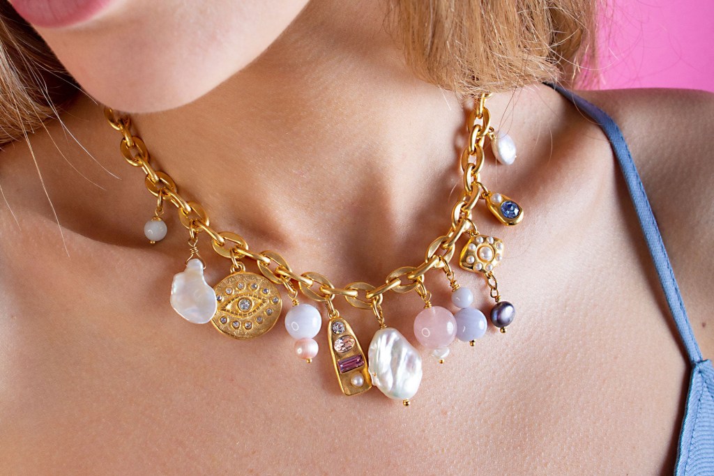 A woman's neck showing a gold necklace with charms on it 