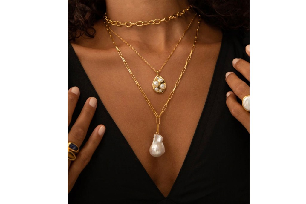 A woman's neck with layered necklaces and hands with rings 