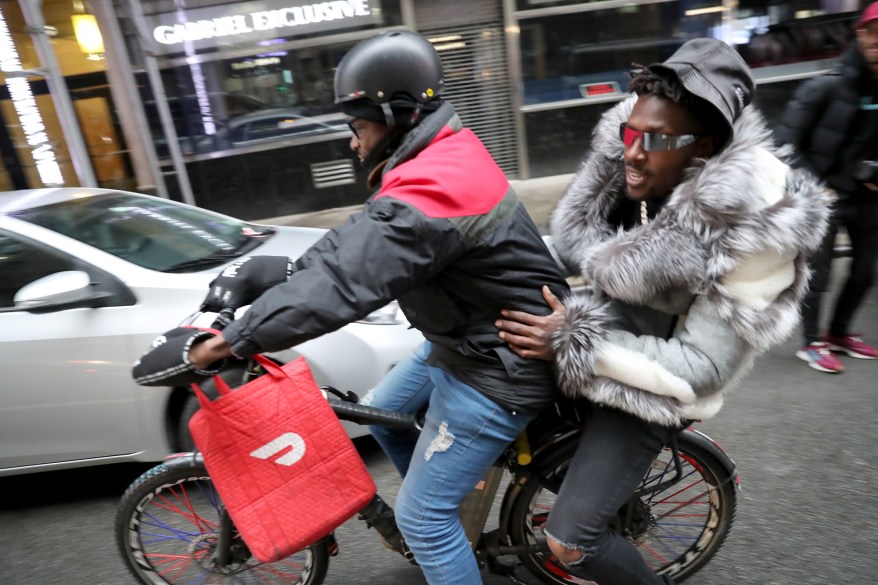 Brown catching a ride with a DoorDash delivery cyclist.